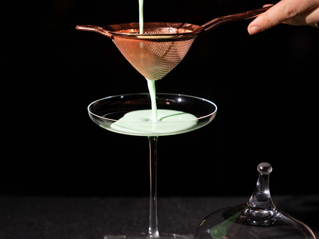 Ristorante gourmet in Val di Fassa: il Mirage al Latemar Cocktail verde viene filtrato in un bicchiere da cocktail su sfondo nero