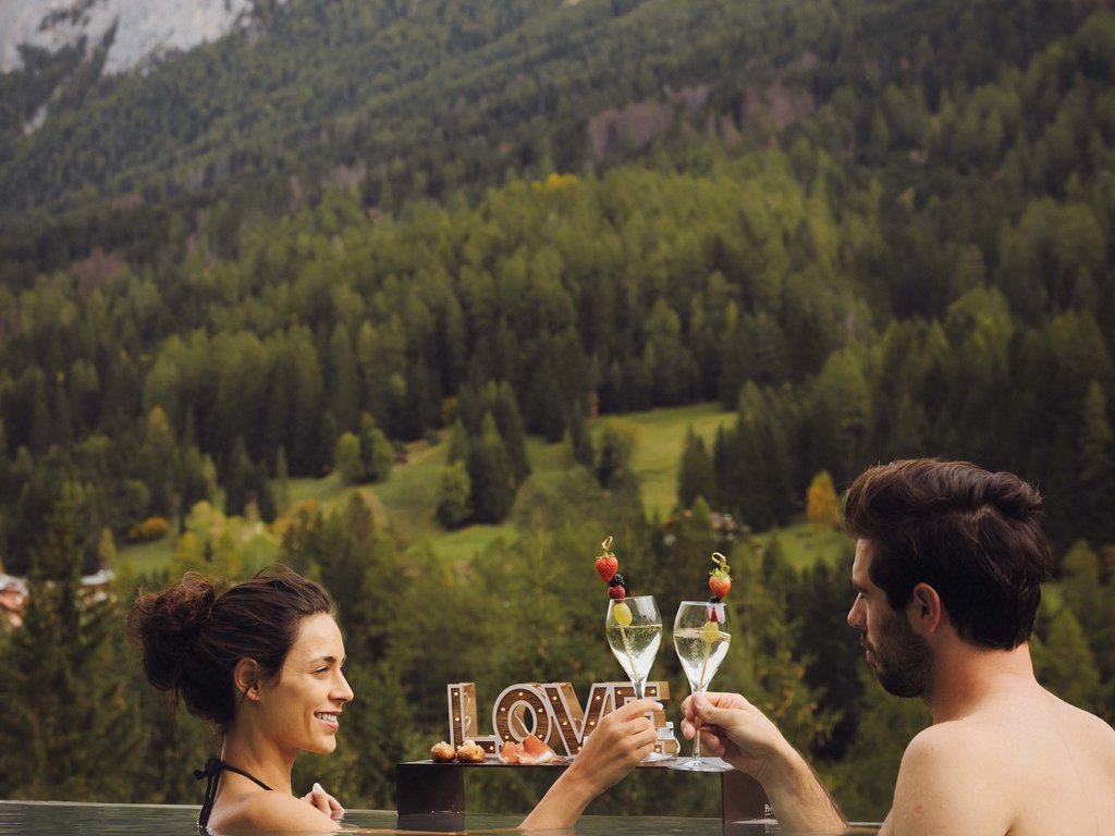 Moena, alberghi da sogno, panorama? C’è l’Hotel Latemar! Coppia si brinda in piscina con vista sulle montagne