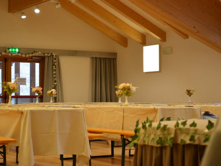 Dalla webcam il Latemar è bello, ma dal vivo è un sogno! Sala con tavoli apparecchiati e fiori in vaso in un ambiente con travi in legno