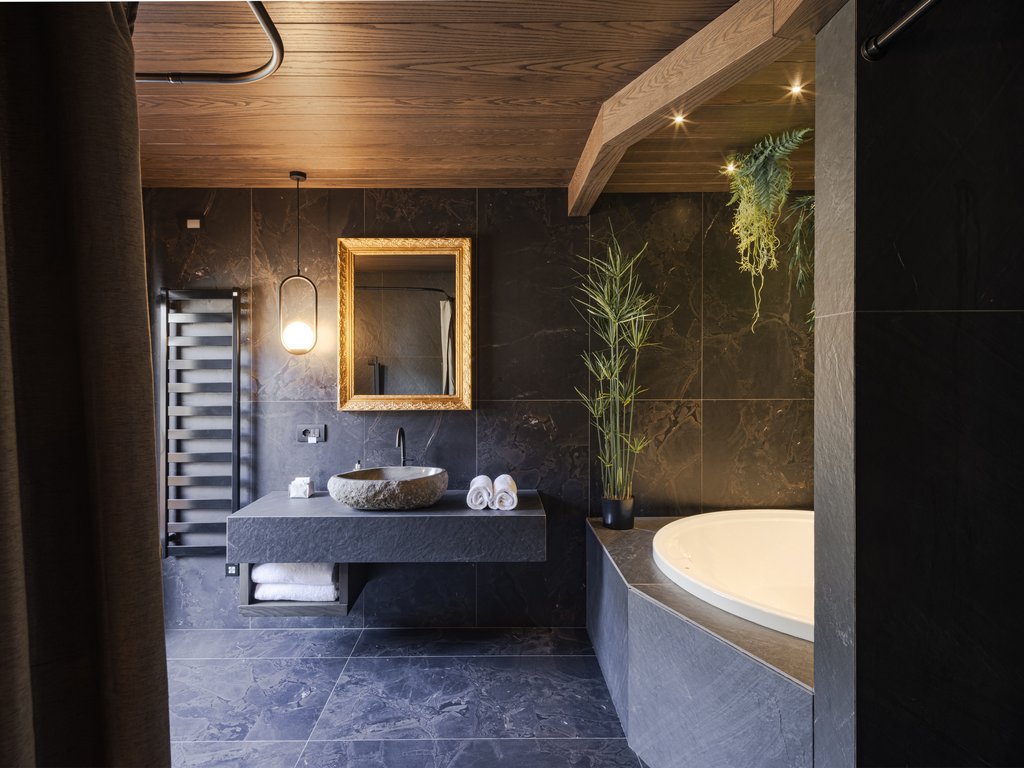 Hotel Latemar mit Dolomitenblick Modernes Badezimmer mit runder Badewanne, steinwaschbecken und grünen Pflanzen