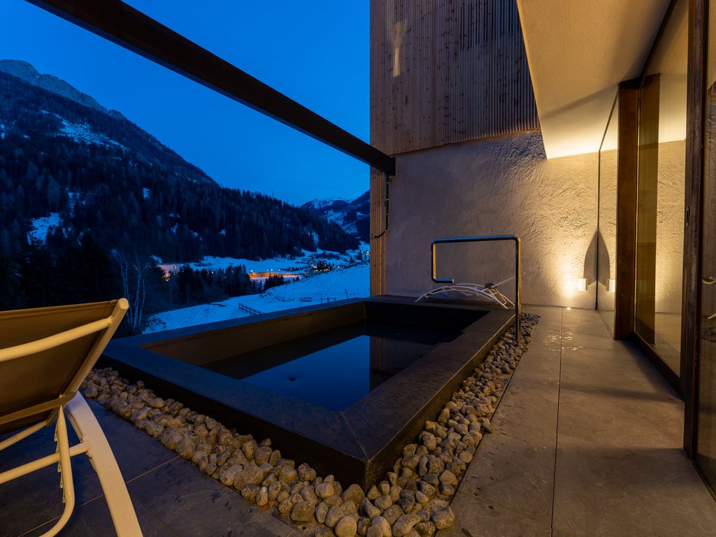 Val di Fassa in estate o inverno? Il relax non ha tempo! Area vasca termale esterna con vista panoramica montagna al crepuscolo