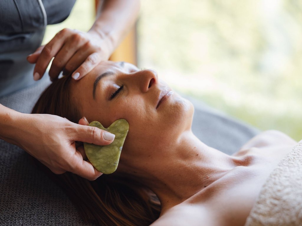 Trattamenti Latemar Signature: un mondo di benessere Donna riceve massaggio facciale con gua sha in ambiente rilassante