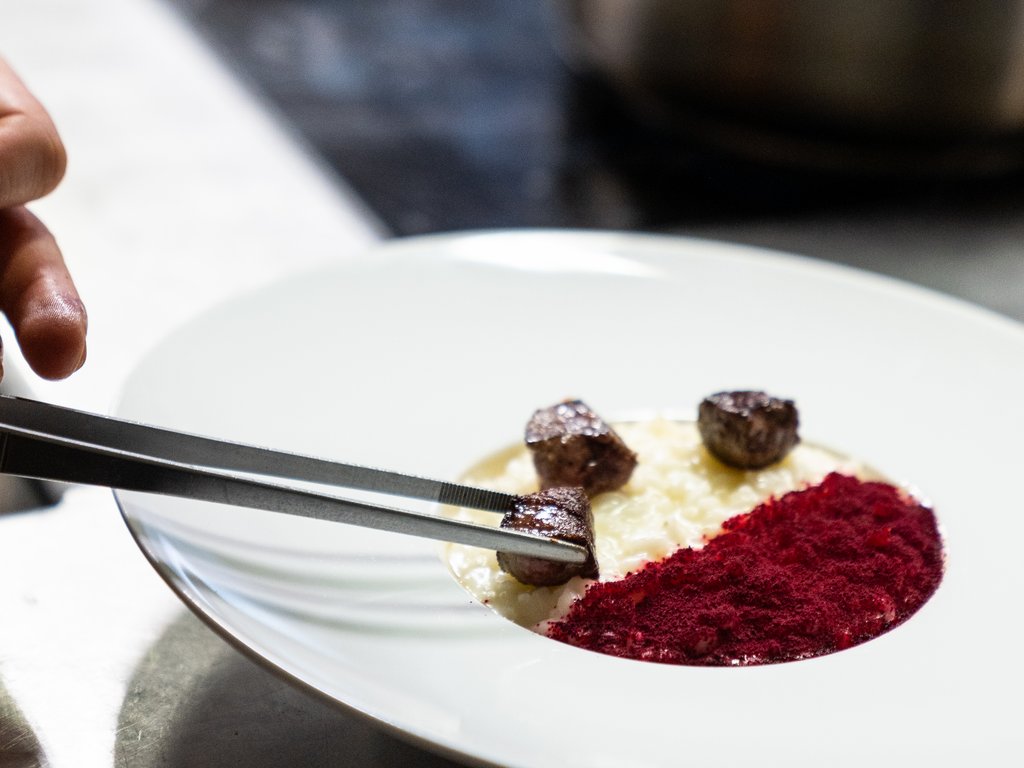 Ristorante gourmet in Val di Fassa: il Mirage al Latemar Chef sistema cubetti di carne su piatto creativo con crema e polvere rossa