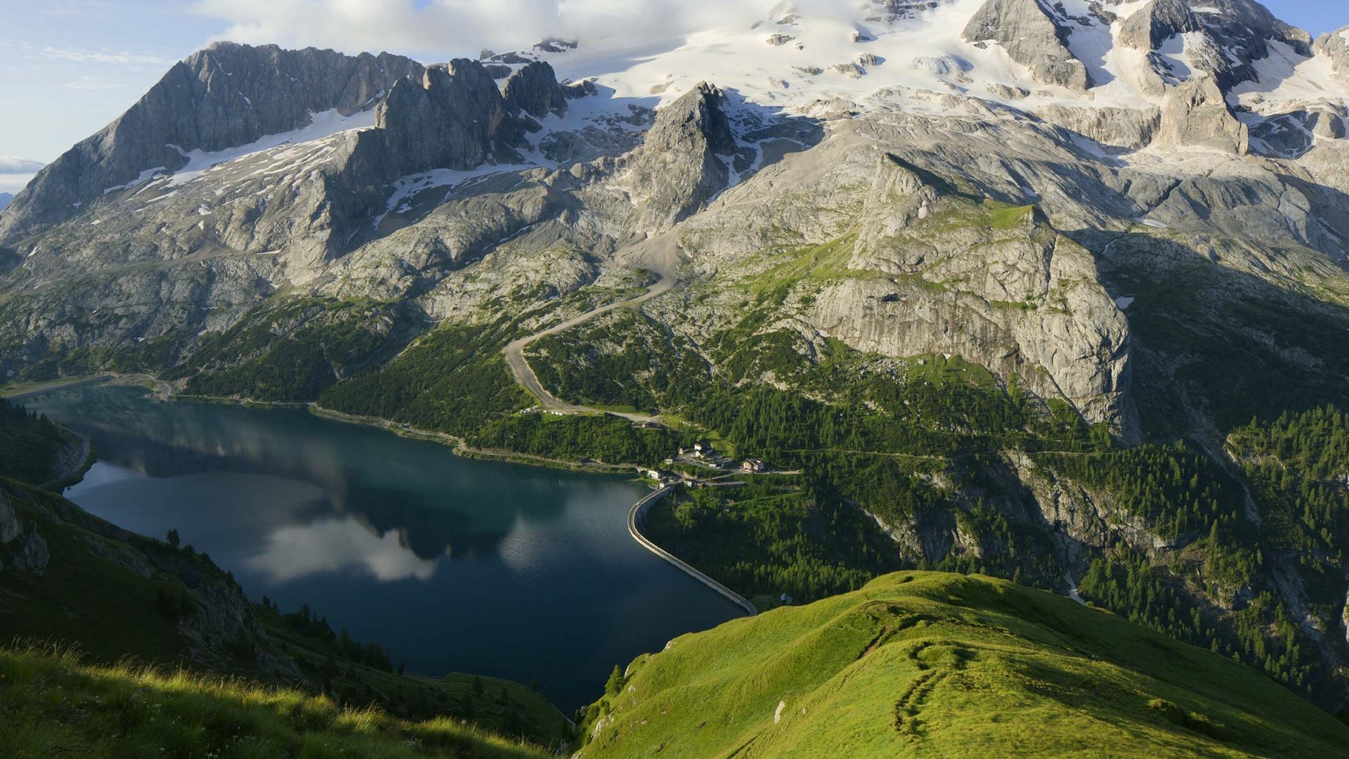 Val di Fassa: dove dormire e vivere vacanze sostenibili Lago montano con montagne innevate e verde paesaggio alpino
