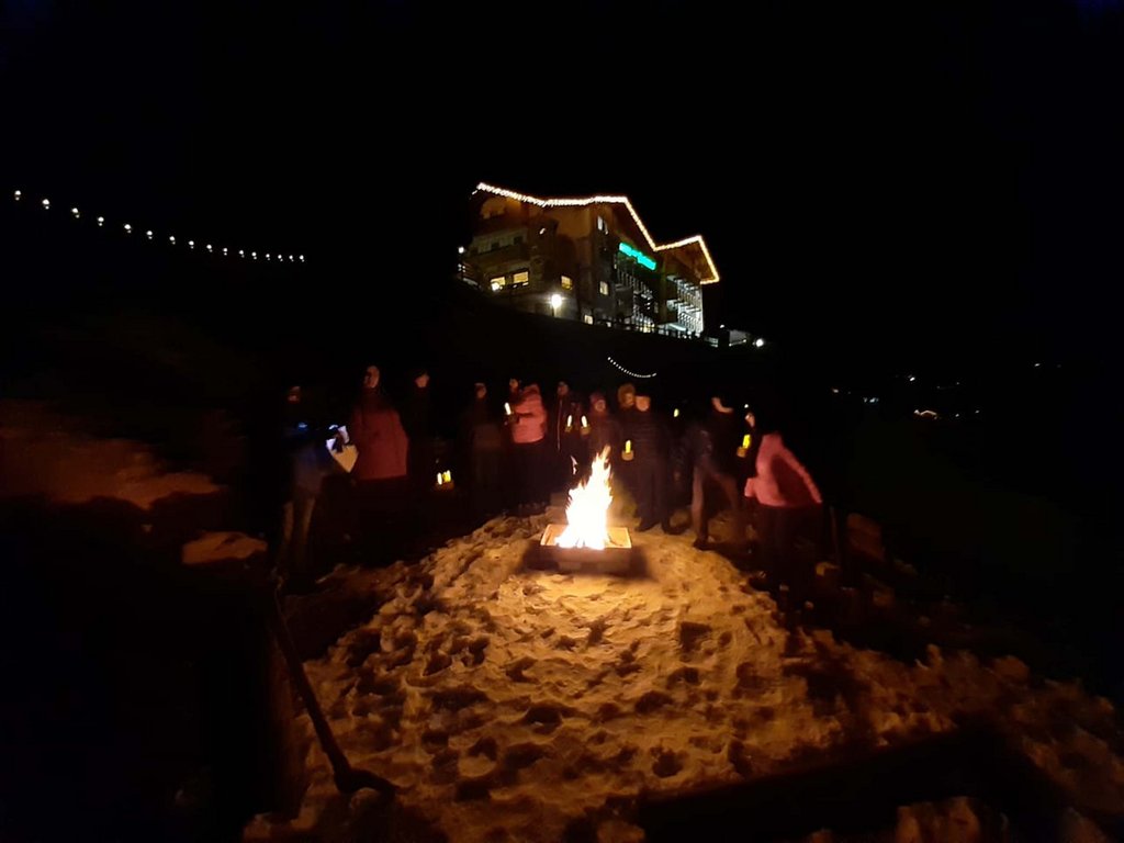 Passeggiate invernali in Val di Fassa: Hotel Latemar Persone radunate intorno a un falò sulla neve di notte