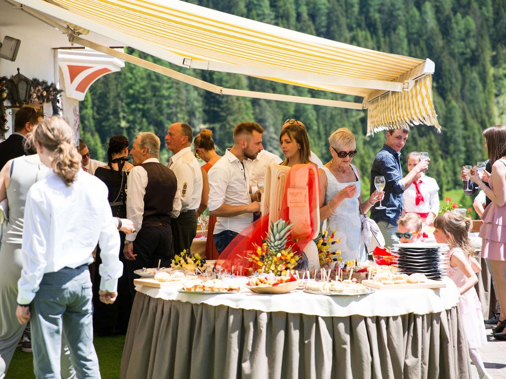 Dalla webcam il Latemar è bello, ma dal vivo è un sogno! Persone a un buffet all'aperto in un evento soleggiato con montagna sullo sfondo