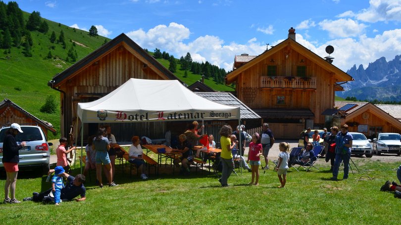La pista ciclabile in Val di Fassa? C’è molto di più! Persone riunite sotto una tenda bianca davanti a baite in montagna