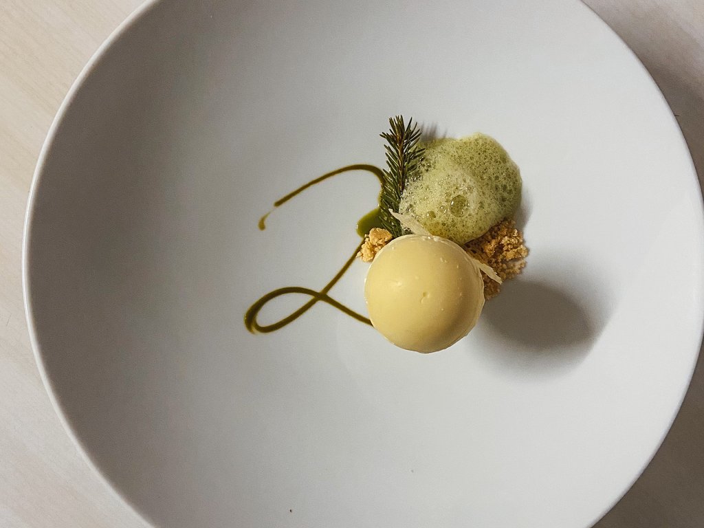 Ristorante gourmet in Val di Fassa: il Mirage al Latemar Dessert gourmet con mousse rotonda, decorazione verde e schiuma su piatto bianco