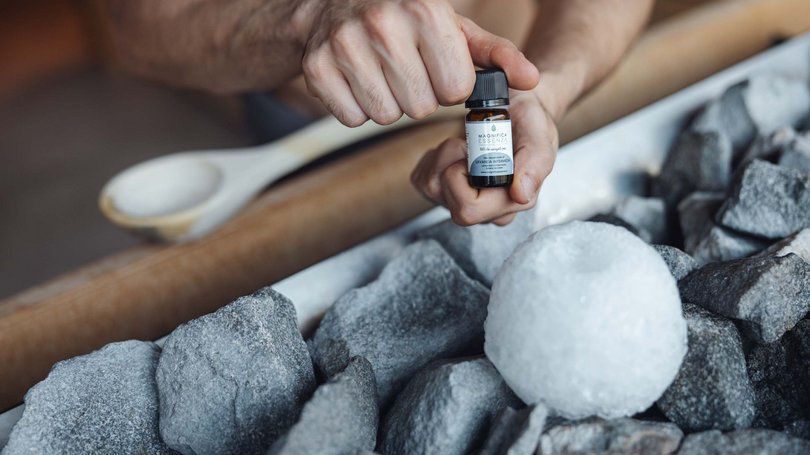 Escursioni da Moena e molto altro: il nostro programma Mano che tiene una bottiglia di olio essenziale vicino a pietre e un pezzo di ghiaccio