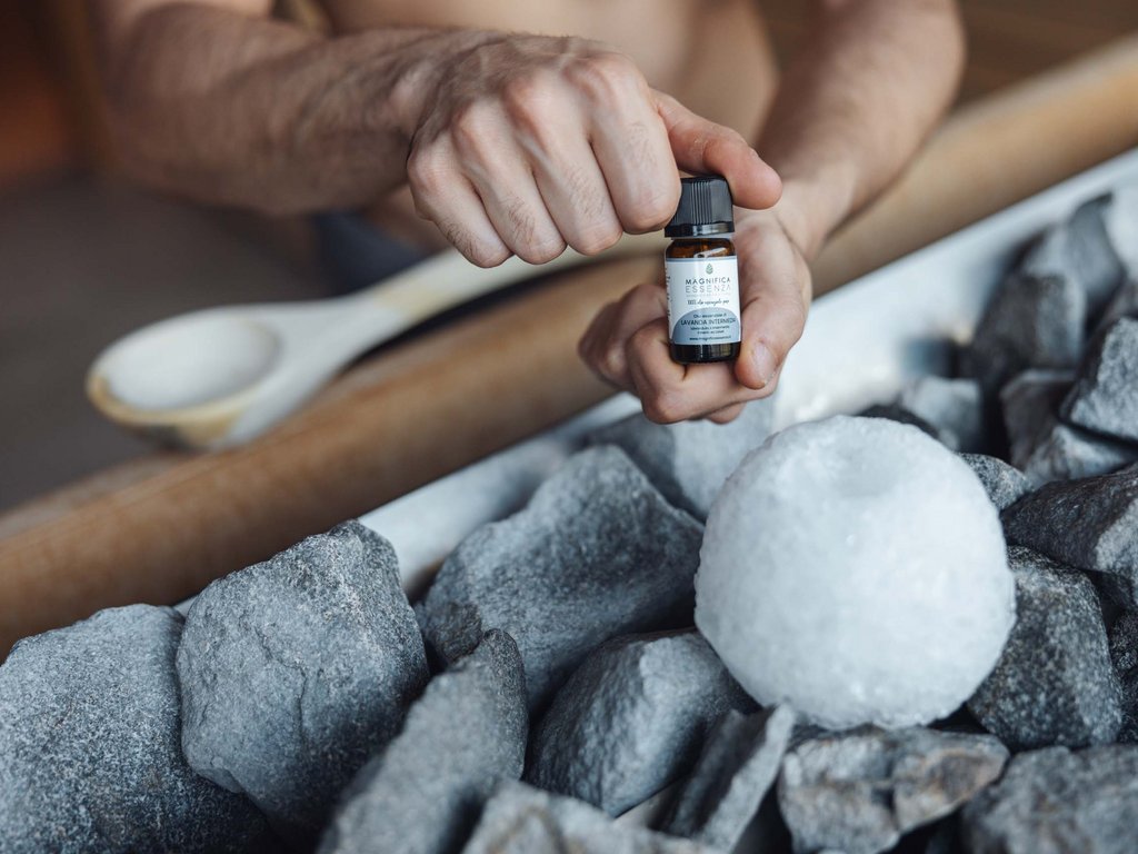 Al Latemar, dopo le passeggiate: relax nella Spa Oniro Mano che tiene una bottiglia di olio essenziale vicino a pietre e un pezzo di ghiaccio