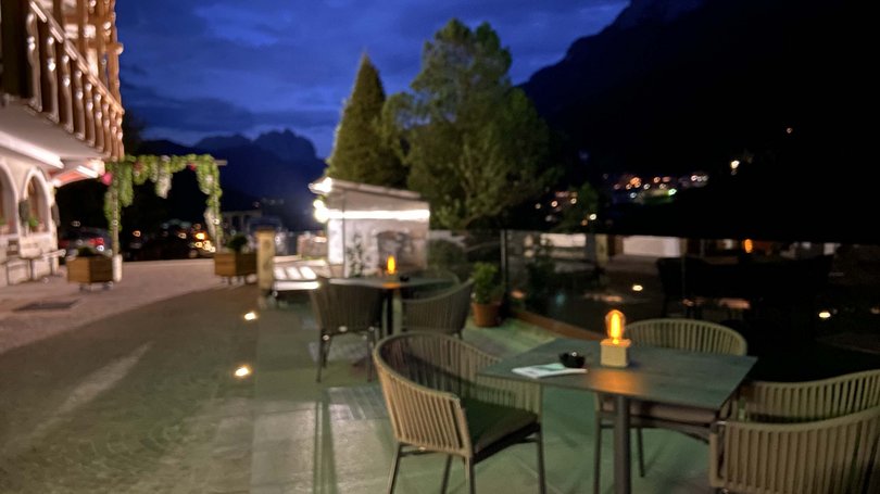 Moena, alberghi da sogno, panorama? C’è l’Hotel Latemar! Terrazza esterna con tavoli e sedie illuminate di sera vicino a un edificio e alberi