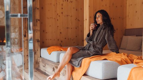 Meteo, Moena, Soraga, Latemar: tutto nella nostra gallery Donna in accappatoio grigio che beve bevanda, seduta in ambiente in legno tipico di spa
