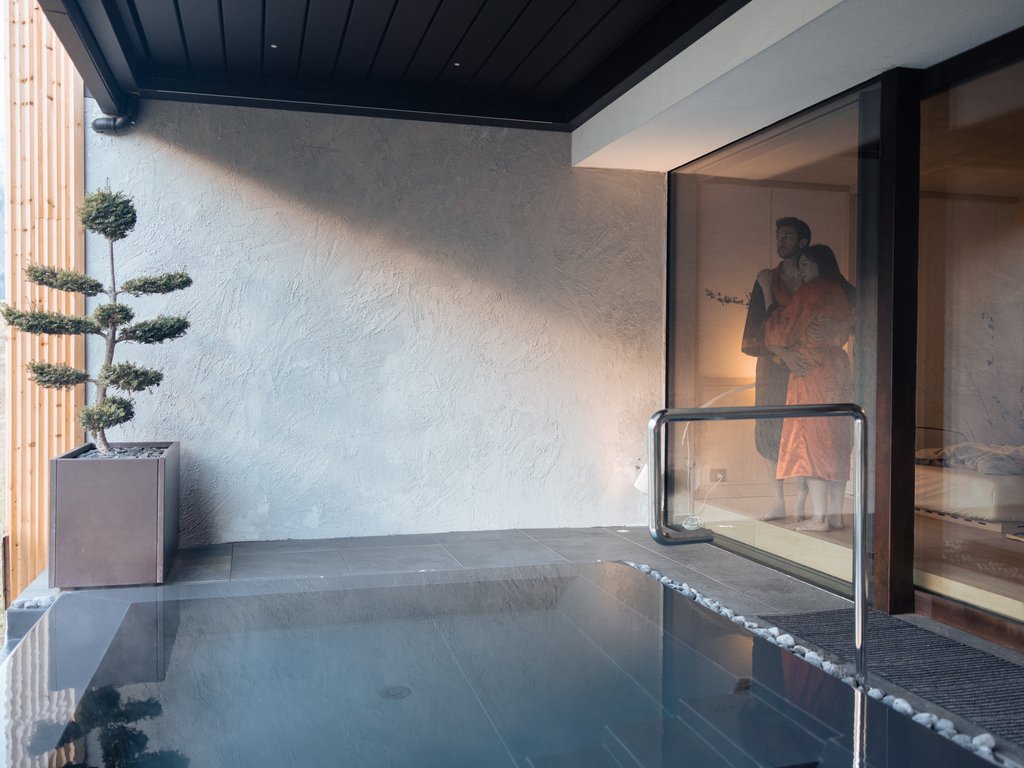Val di Fassa in estate o inverno? Il relax non ha tempo! Piscina moderna all'aperto con coppia che si abbraccia dietro una finestra