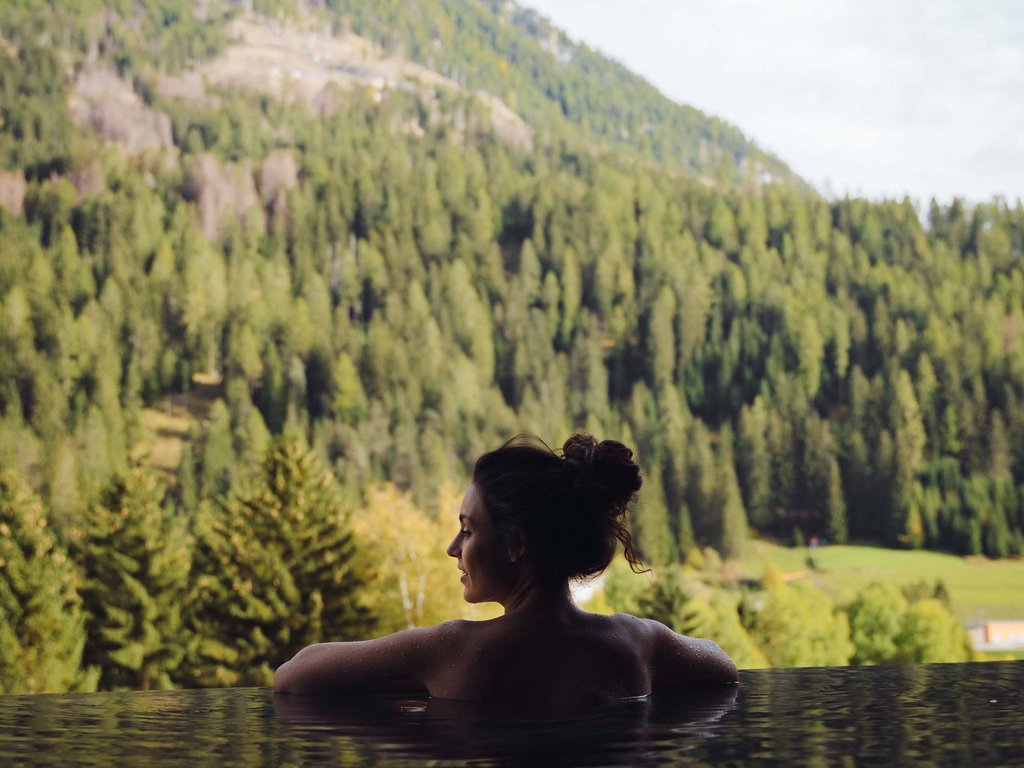Val di Fassa: dove dormire e vivere vacanze sostenibili Donna che si rilassa in una piscina con vista sulle montagne verdi