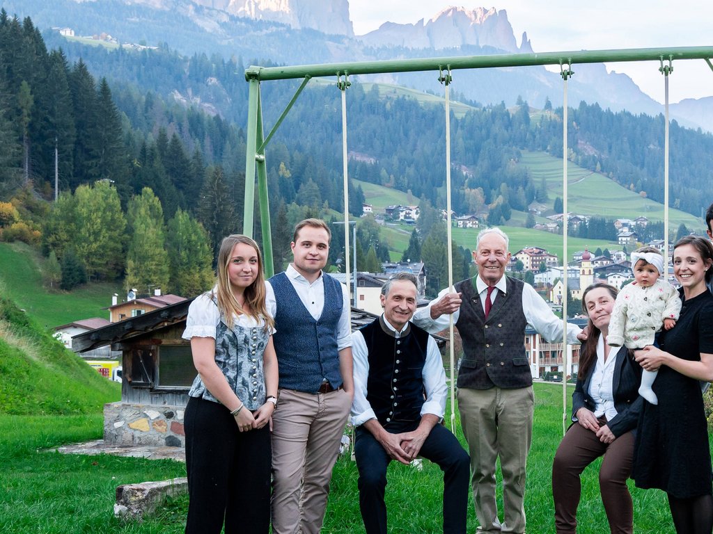 Hotel a Soraga: passione di famiglia Gruppo familiare sorridente in abiti tradizionali con sfondo di montagne e case