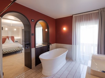 Hotel per disabili in Val di Fassa: il Latemar Bagno moderno con vasca bianca, specchi e camera da letto visibile