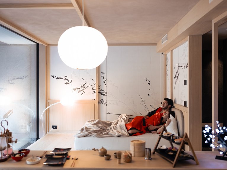 Val di Fassa in estate o inverno? Il relax non ha tempo! Coppia che si rilassa in una stanza moderna con cibo e luce soffusa