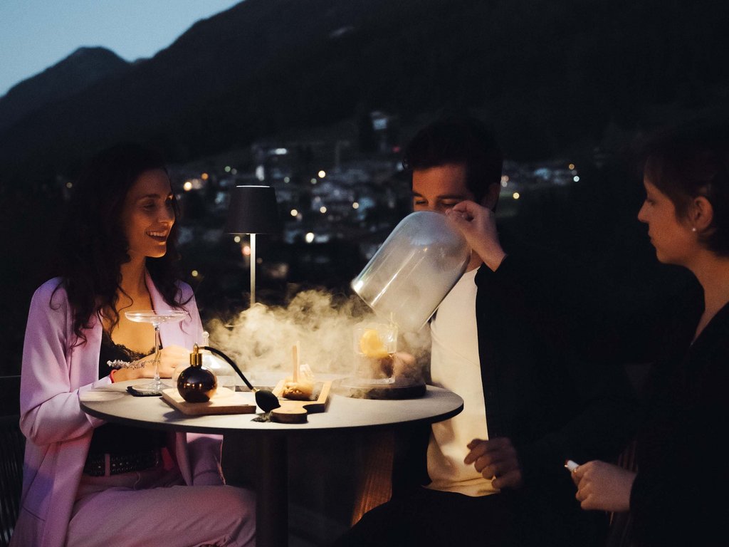 Val di Fassa e ciclabile: da ammirare dal cocktail & tea bar Tre persone a un tavolo all'aperto di sera con montagne sullo sfondo