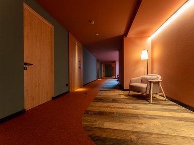 Hotel per disabili in Val di Fassa: il Latemar Corridoio di hotel con pavimento in legno, moquette rossa e poltrona illuminata