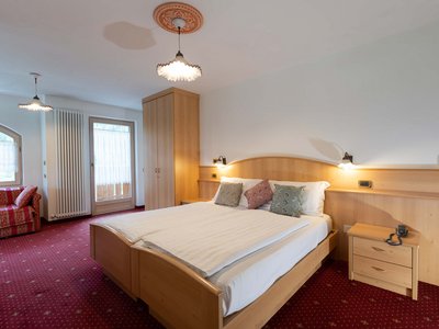 Hotel a 3 stelle superior a Soraga in Val di Fassa: camere & suites Camera da letto con letto matrimoniale, armadio, divano rosso e moquette rossa