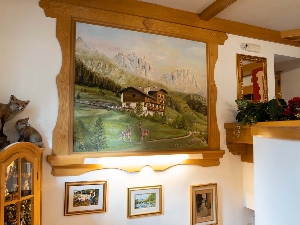 Hotel a Soraga: passione di famiglia Interno con dipinti di paesaggi montani su parete in legno
