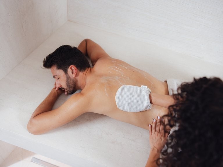 Il rituale dell’hammam al Latemar Hotel Uomo sdraiato mentre riceve un massaggio alla schiena con guanto esfoliante