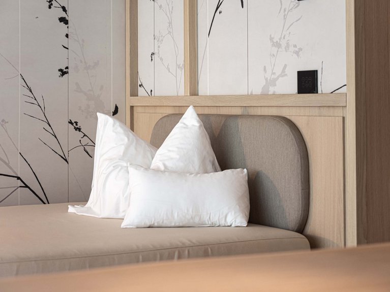 Val di Fassa in estate o inverno? Il relax non ha tempo! Letto moderno con cuscini bianchi e testiera in tessuto beige