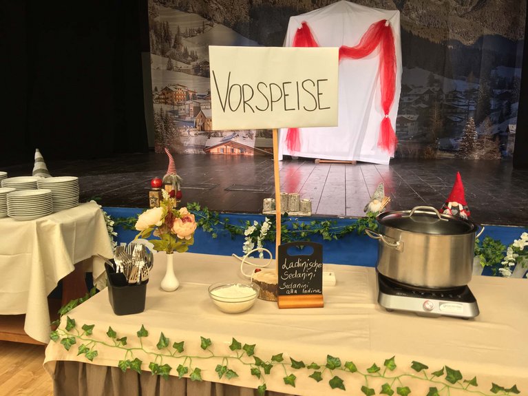Dalla webcam il Latemar è bello, ma dal vivo è un sogno! Tavolo con piatti, posate, fiori e una pentola con cartello Vorspeise