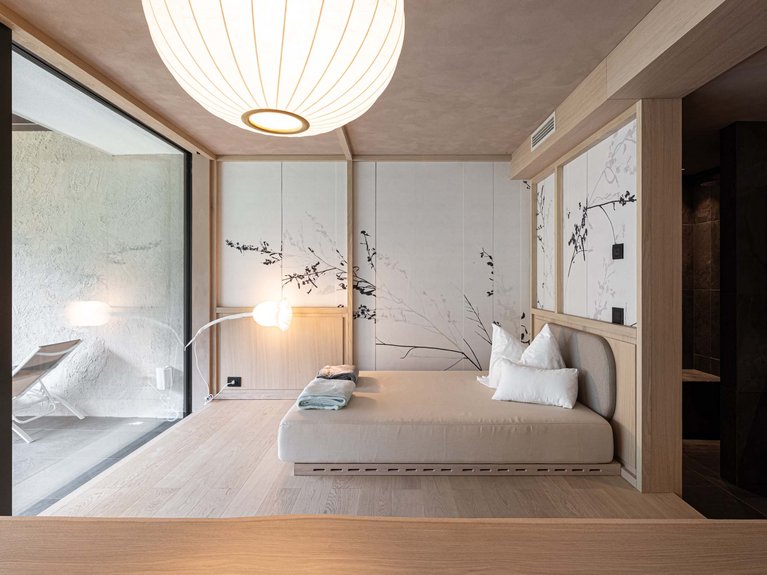 Val di Fassa in estate o inverno? Il relax non ha tempo! Camera moderna con letto minimalista, lampada e pareti decorate