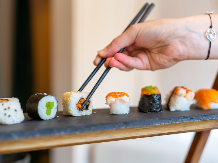 Val di Fassa in estate o inverno? Il relax non ha tempo! Mano che prende un sushi con bacchette da un vassoio