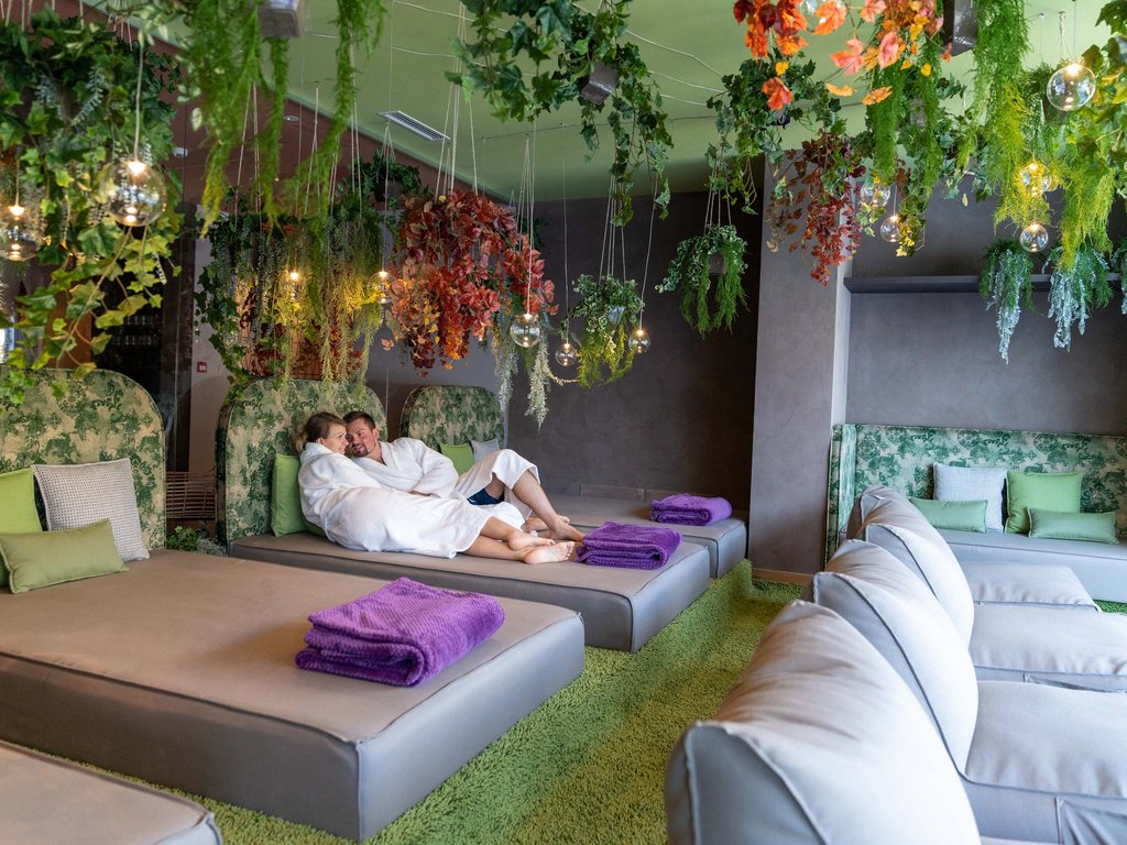 Val di Fassa: dove dormire e vivere vacanze sostenibili Coppia in accappatoi rilassata su lettini in una spa con piante verdi appese