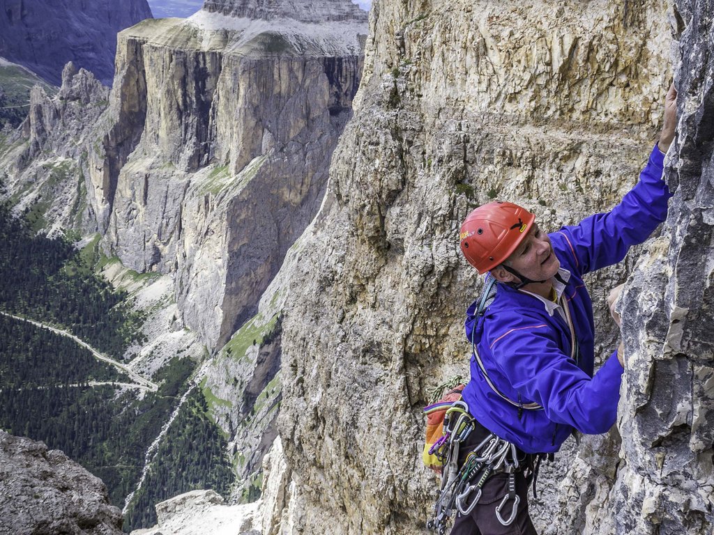 Lago di Soraga e attività estive vicino al Latemar Escursionista con casco rosso che scala una parete di roccia nelle Dolomiti