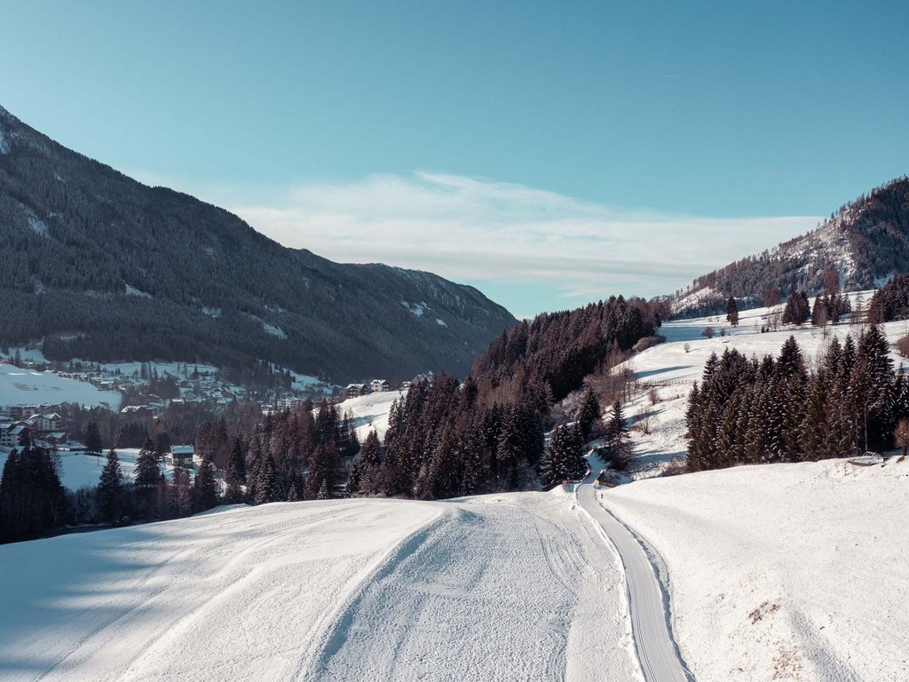 Passeggiate invernali in Val di Fassa: Hotel Latemar Paesaggio invernale con strada innevata tra montagne e alberi.