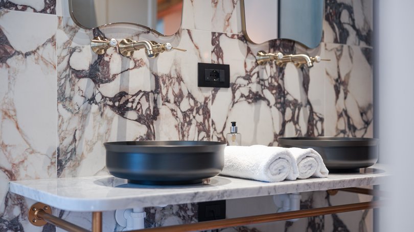Moena, alberghi da sogno, panorama? C’è l’Hotel Latemar! Lavabi neri moderni con rubinetti dorati su marmo e asciugamani bianchi arrotolati
