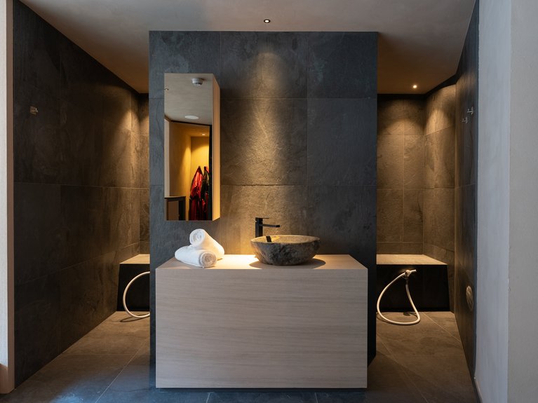 Val di Fassa in estate o inverno? Il relax non ha tempo! Bagno moderno con lavabo in pietra, asciugamani bianchi e pareti scure