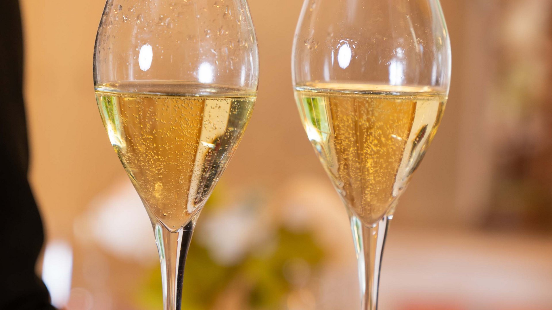 In Val di Fassa in inverno e in estate si brinda col vino! Due calici di vino bianco frizzante su un vassoio nero