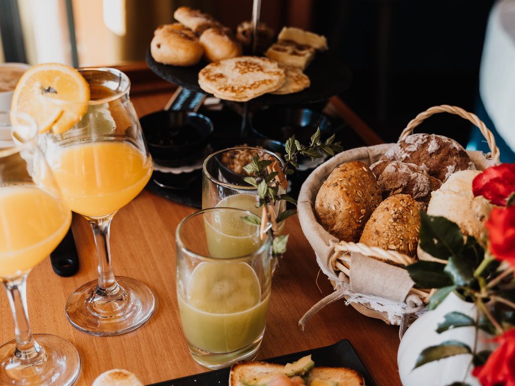 Ristorante a Soraga di Fassa: Mirage con #latermarview Colazione con toast, succhi, pane, affettati e fiori rossi su tavolo di legno