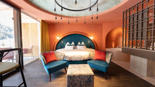 Hotel Latemar mit Dolomitenblick Modernes Schlafzimmer mit blauen Sesseln, rundem Bett und großem Fenster