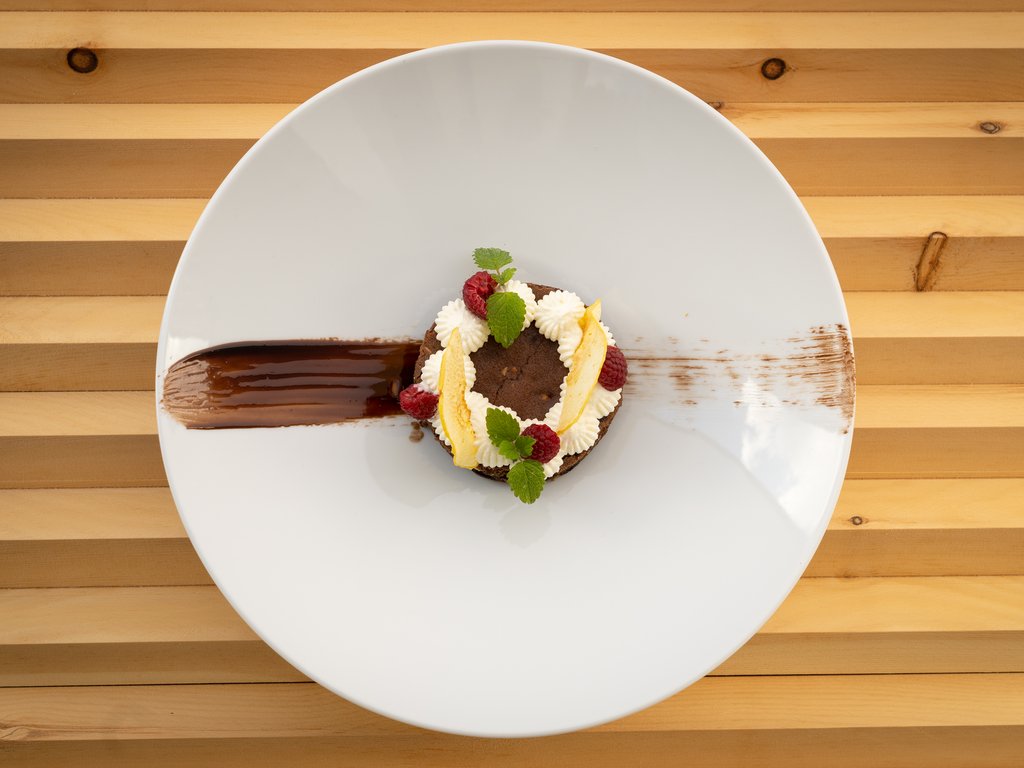 Ristorante a Soraga di Fassa: Mirage con #latermarview Dessert al cioccolato con crema, lamponi e foglie di menta su piatto bianco