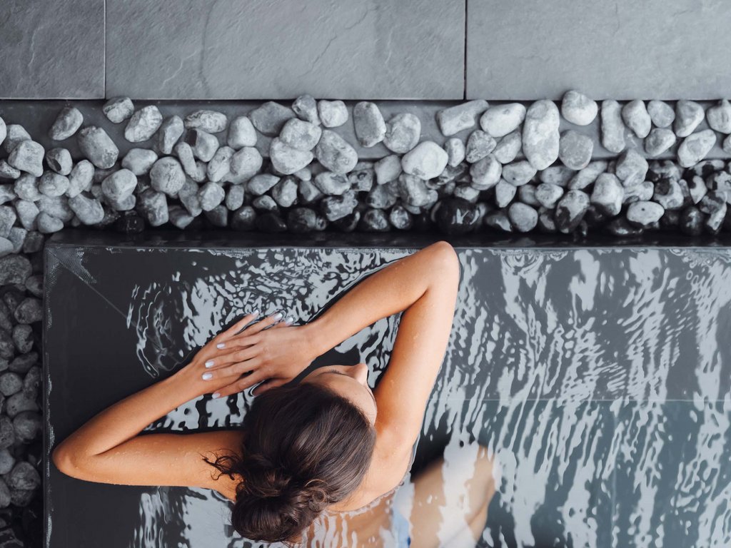 Val di Fassa in estate o inverno? Il relax non ha tempo! Donna che si rilassa in una piscina con lastre e pietre bianche