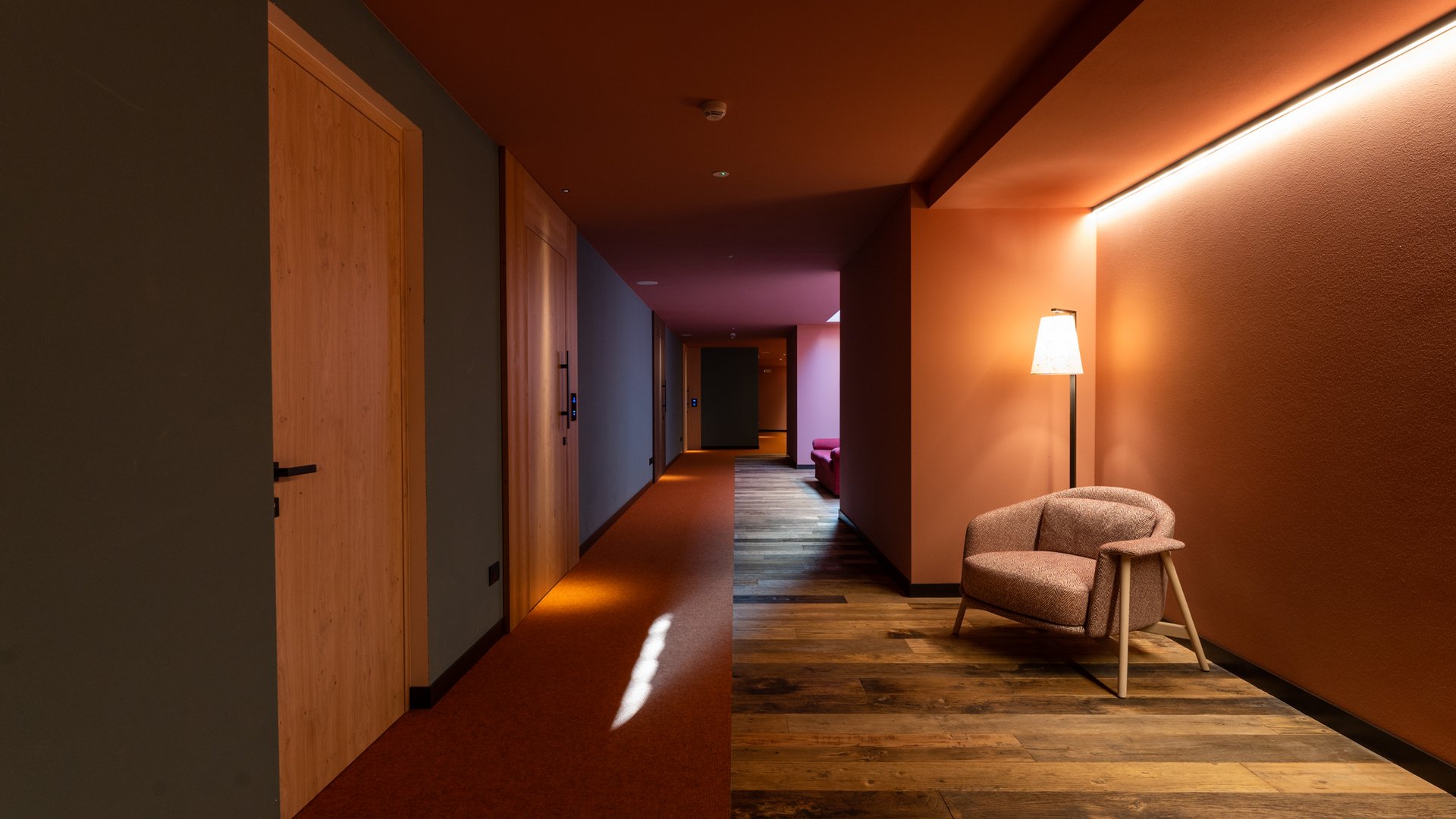 Hotel per disabili in Val di Fassa: il Latemar Corridoio moderno con poltrona, illuminazione calda e pavimento legno
