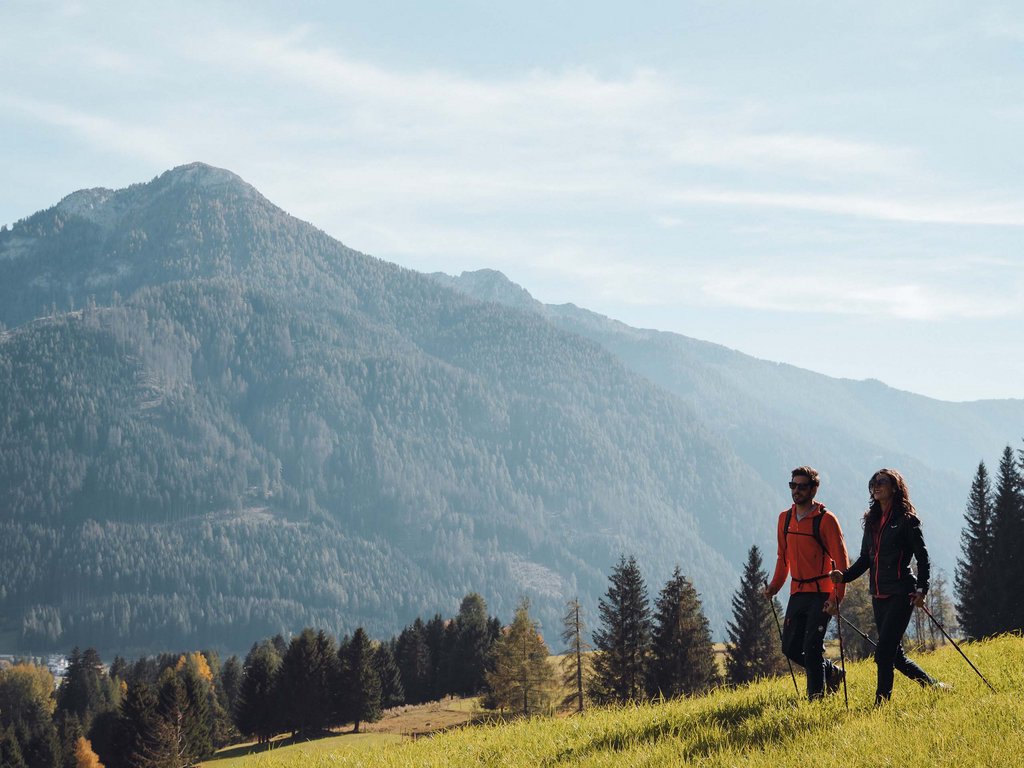 Estate in Val di Fassa, preceduta da una primavera da sogno Due escursionisti che camminano su un prato verde con montagne sullo sfondo