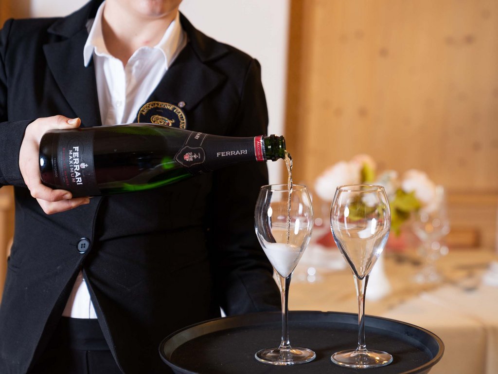 Ristorante a Soraga di Fassa: Mirage con #latermarview Cameriere che versa vino spumante Ferrari in due bicchieri da flûte