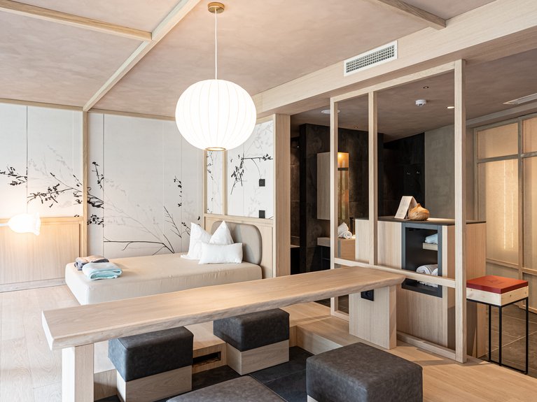 Val di Fassa in estate o inverno? Il relax non ha tempo! camera moderna con letto basso, tavolo in legno e sedute imbottite