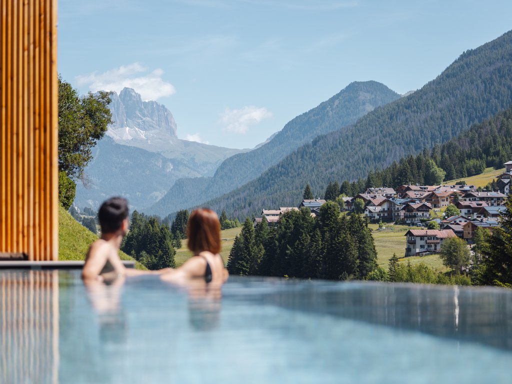 Al Latemar, dopo le passeggiate: relax nella Spa Oniro Coppia in piscina a sfioro con vista sulle montagne e un villaggio