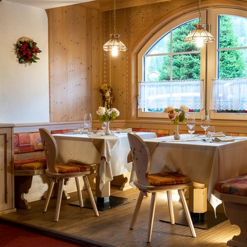 Ristorante a Soraga di Fassa: Mirage con #latermarview Sala da pranzo elegante in legno con tavoli apparecchiati e vista sulle montagne