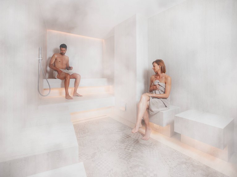 Il rituale dell’hammam al Latemar Hotel Due persone in accappatoi sedute in una sauna fumosa moderna