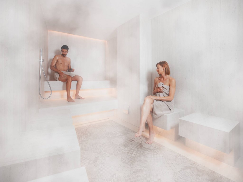 Al Latemar, dopo le passeggiate: relax nella Spa Oniro Due persone in accappatoi sedute in una sauna fumosa moderna