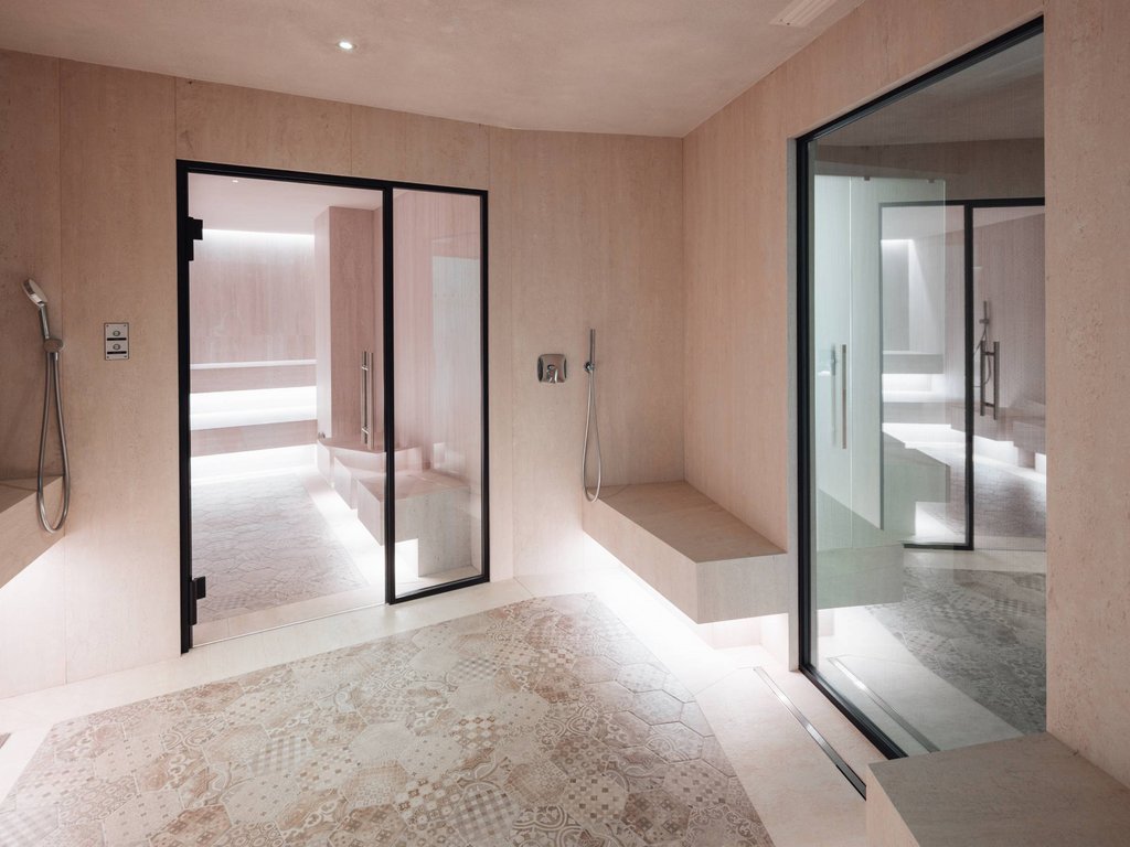 Al Latemar, dopo le passeggiate: relax nella Spa Oniro Interno di una sauna moderna con pareti in pietra chiara e pavimento decorato