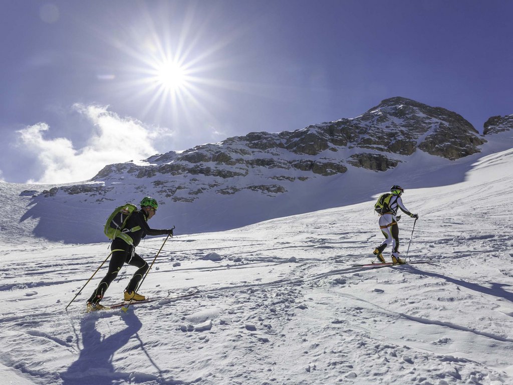 Passeggiate invernali in Val di Fassa: Hotel Latemar Due sciatori con zaini che salgono una montagna innevata sotto il sole